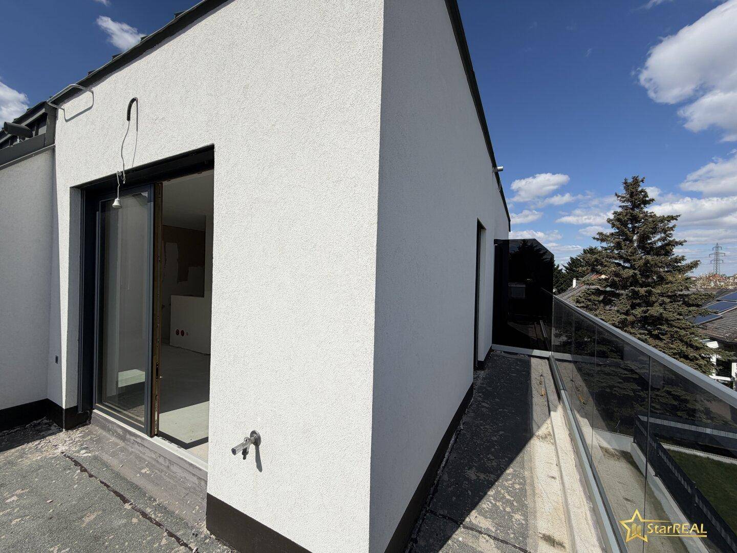 Geräumige Dachterrasse mit modernem Glasgeländer und Zugang zum Gebäude.