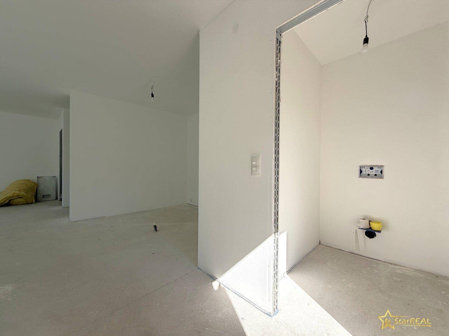 Unfertiger Küchenbereich im Neubau mit vorbereiteten Anschlüssen und viel Tageslicht.