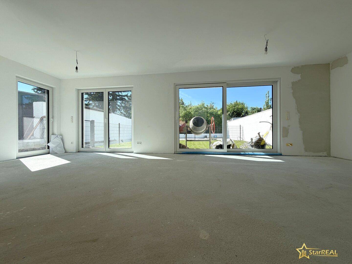 Heller Wohnbereich im Rohbau mit großen Fensterfronten und direktem Zugang zum Garten.