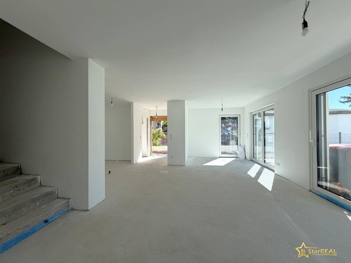 Geräumiger Wohnbereich im Neubau mit Treppenaufgang und großen Fenstern für viel Licht.