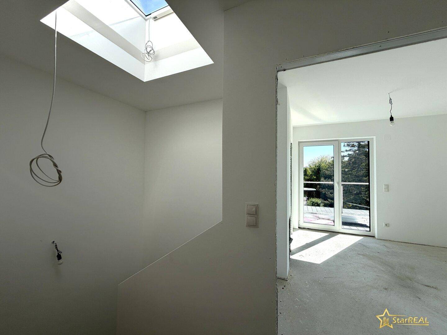Treppenaufgang im Neubau mit Oberlicht und Blick in ein angrenzendes, helles Zimmer.