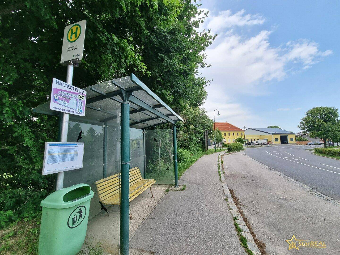 Überdachte Bushaltestelle mit Sitzbank und Mülleimer an einer ländlichen Straße.