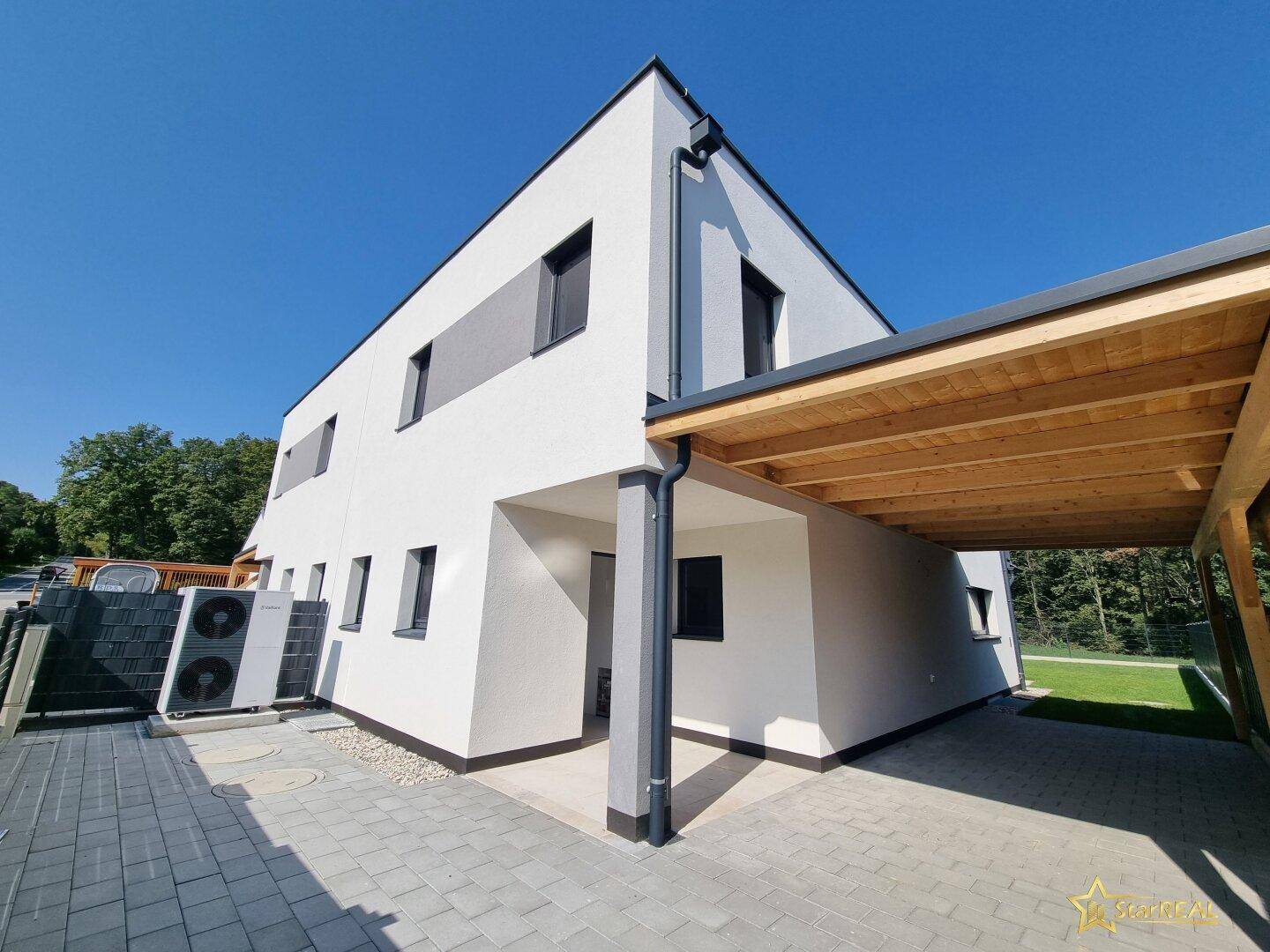 Seitenansicht des Hauses mit Carport, Wärmepumpe und gepflastertem Bereich.