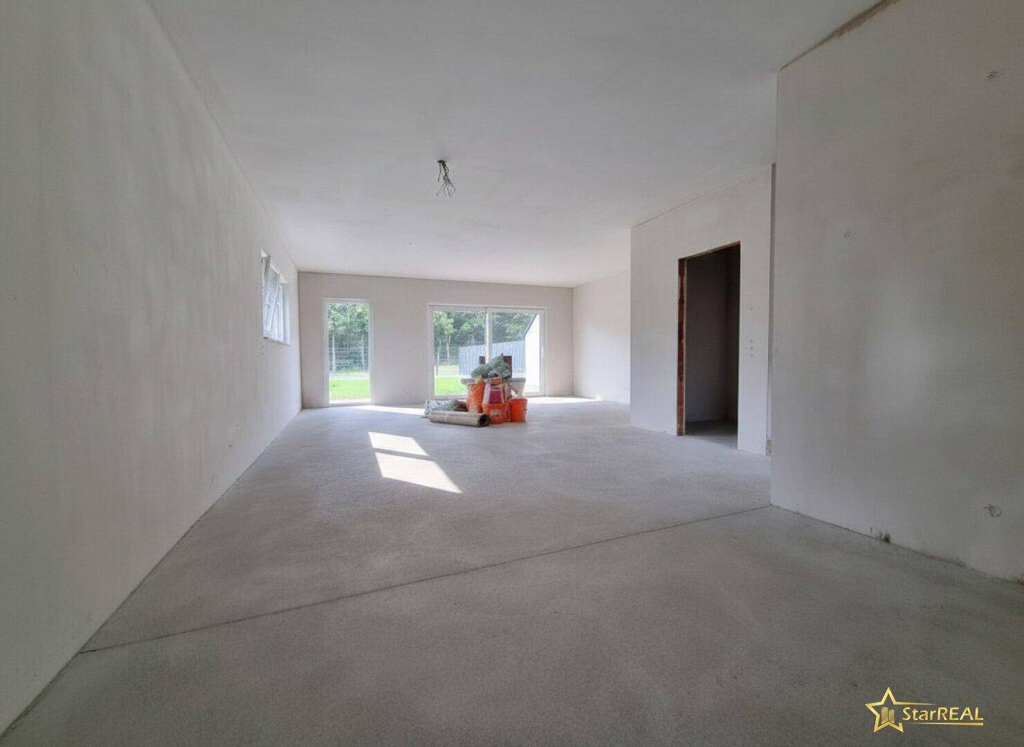 Geräumiges Wohnzimmer im Rohbau mit Betonboden und Zugang zum Garten.