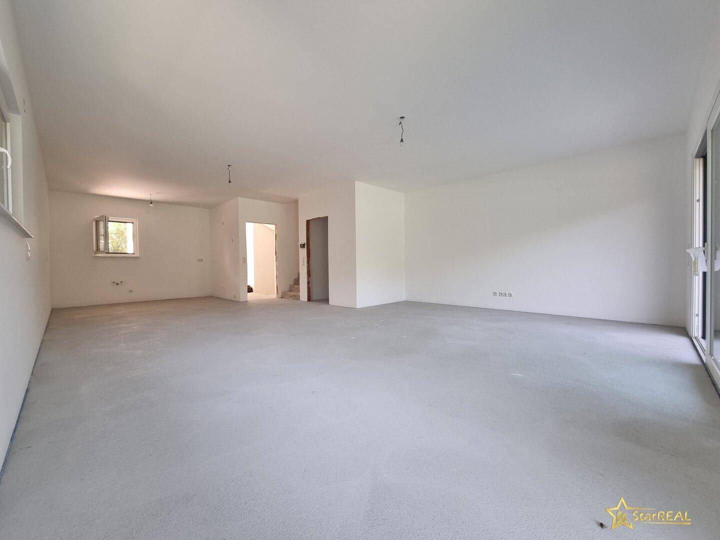 Heller Wohnbereich im Rohbau mit glattem Betonboden und weißen Wänden.