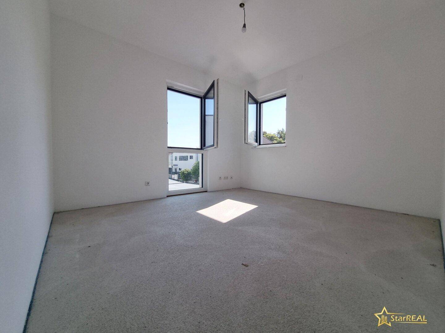 Helles Schlafzimmer im Rohbau mit großen Fenstern und Betonboden.