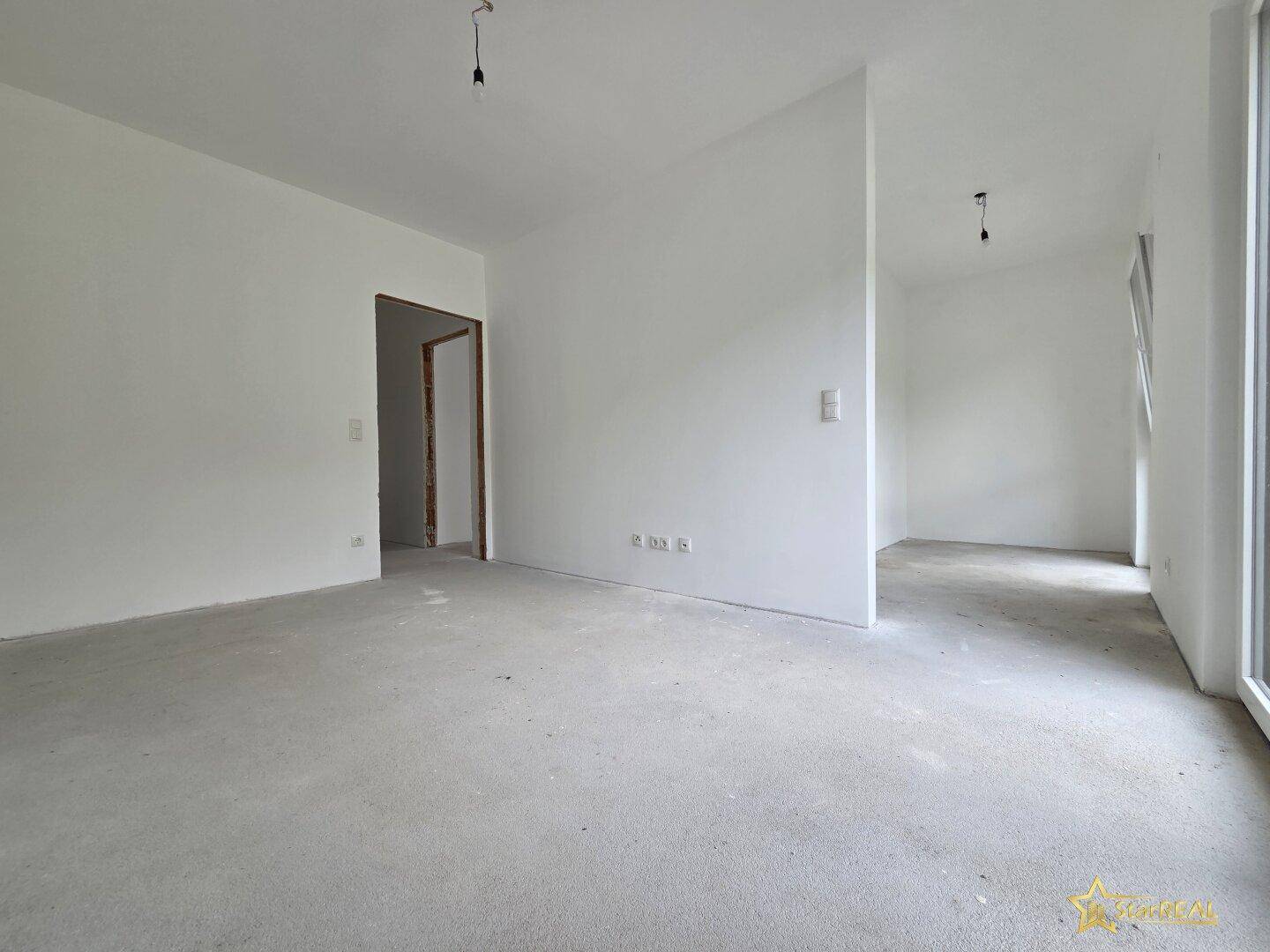 Unfertiger Innenraum mit weißen Wänden und Betonboden, bereit für den Ausbau.