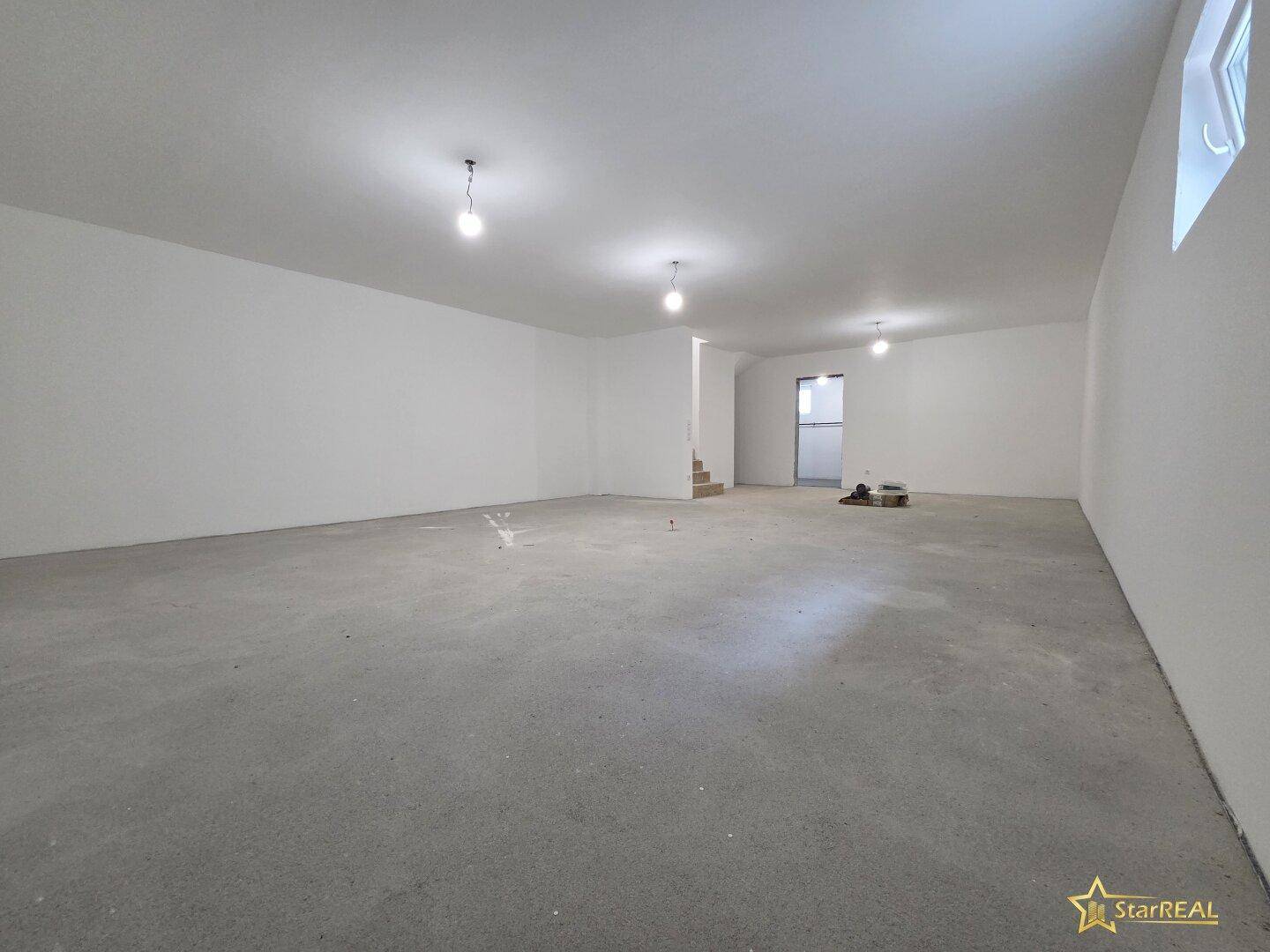 Großer Kellerraum im Rohbau mit Betonboden und einfacher Beleuchtung.