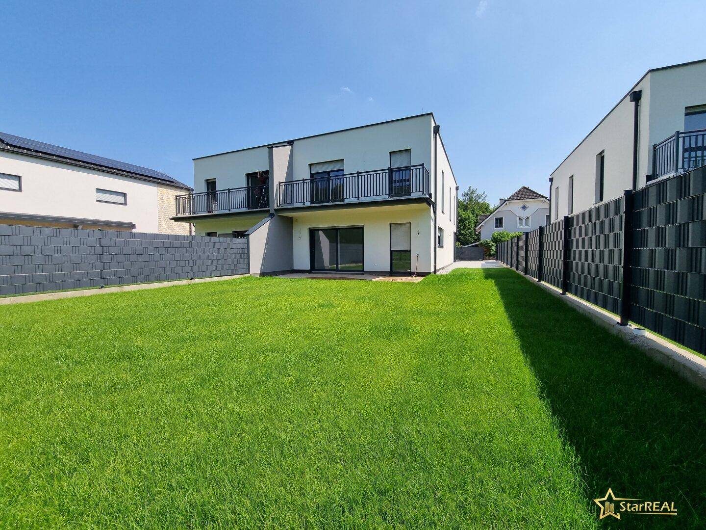 Moderne Doppelhaushälfte mit gepflegtem Rasen, Balkonen und einer Terrasse im Gartenbereich.
