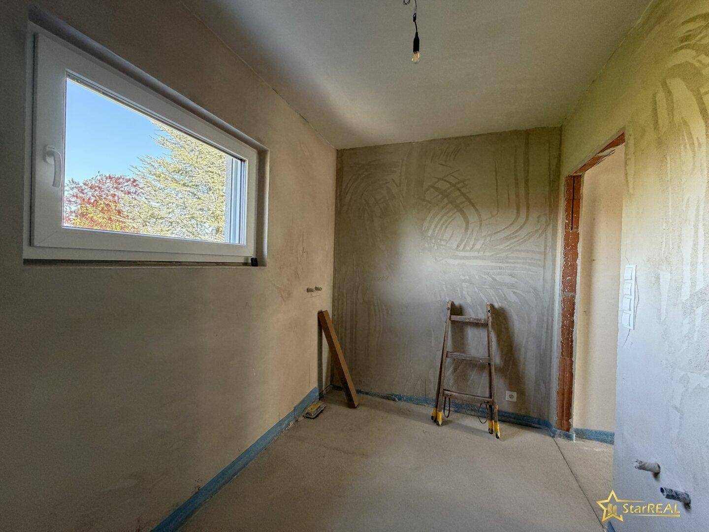 Unfertiges Badezimmer mit Fenster und vorbereiteten Anschlüssen für Sanitärinstallationen.