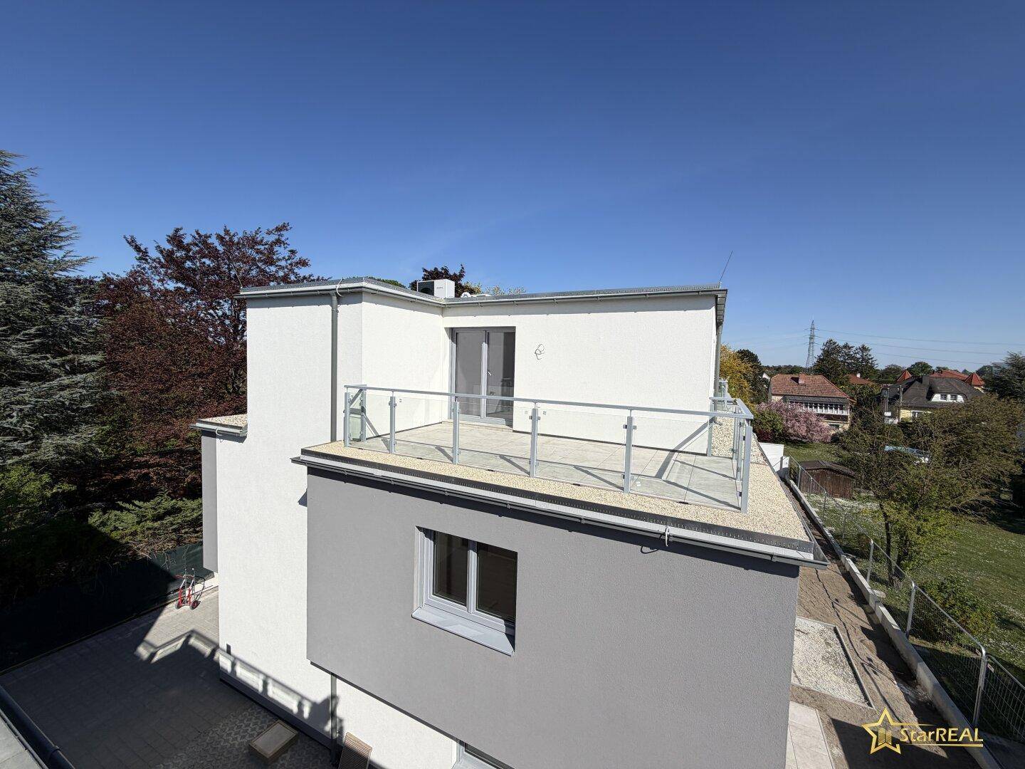 Weitläufige Dachterrasse mit Glasgeländer und Blick auf die Umgebung unter blauem Himmel.