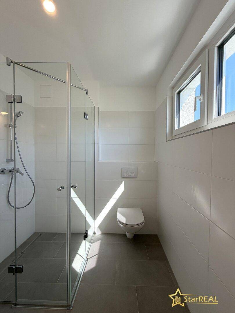 Modernes Badezimmer mit begehbarer Dusche, wandhängendem WC und Fenster.
