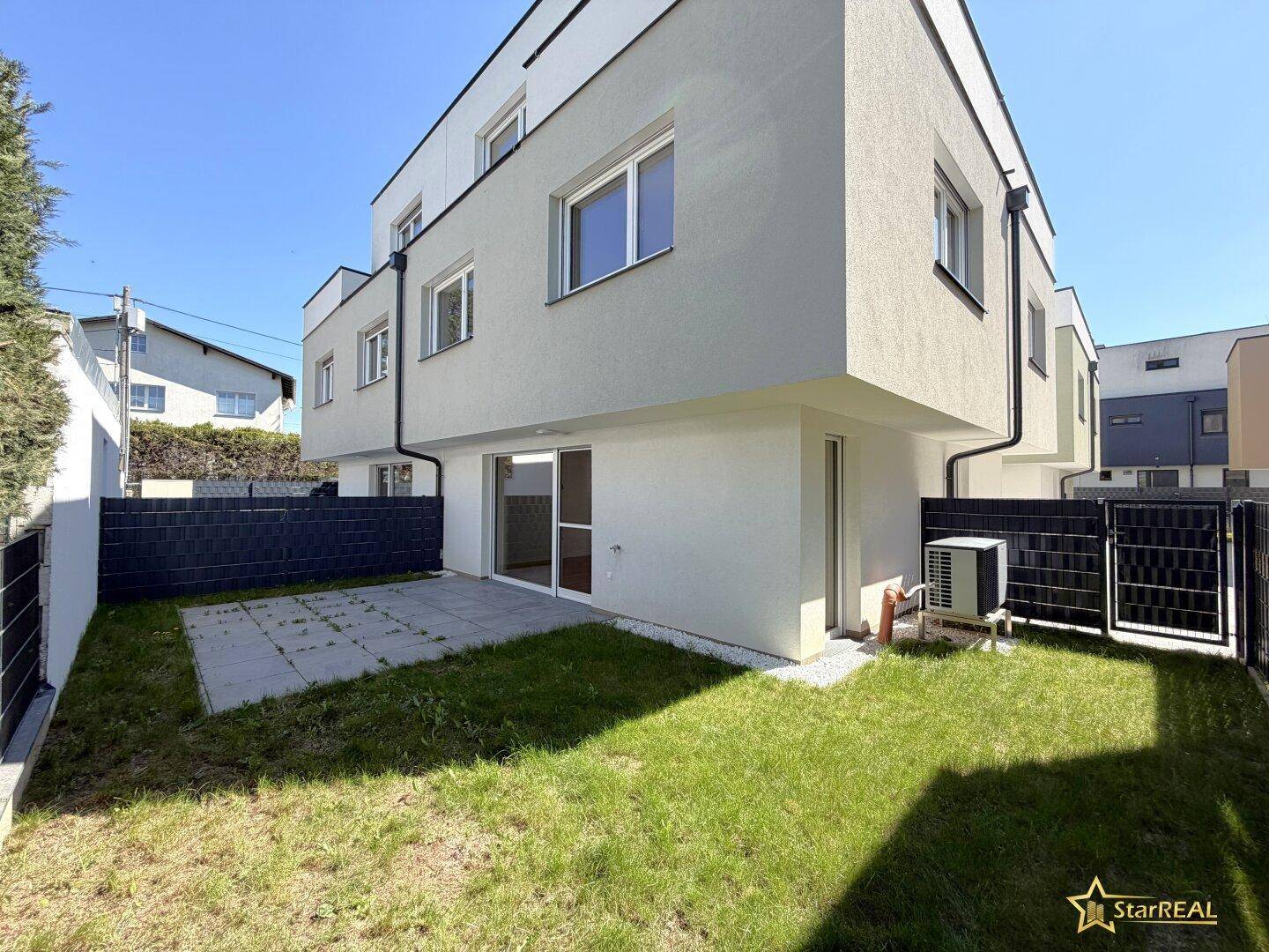 Hinterhof eines Reihenhauses mit kleiner Rasenfläche und gepflasterter Terrasse.