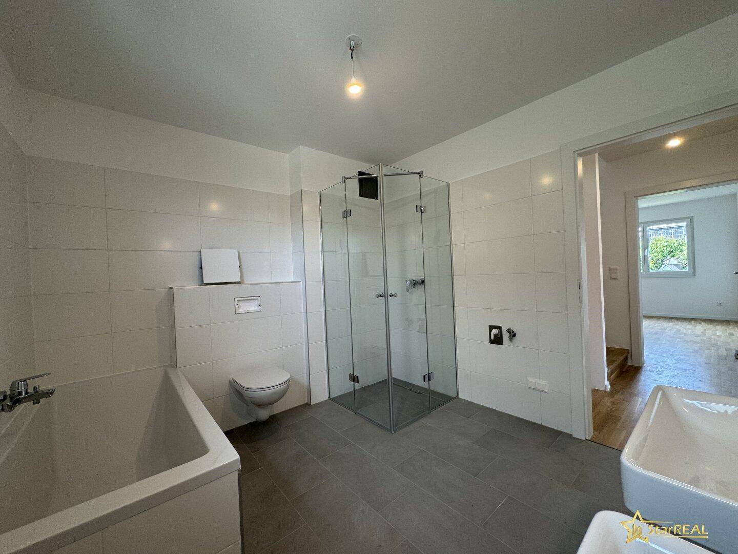 Modernes Badezimmer mit Duschkabine, Badewanne und wandhängendem WC in hellen Fliesen.