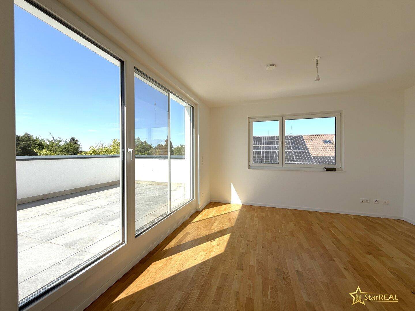 Heller Raum mit großen Fenstern, Zugang zur Dachterrasse und Blick auf Solarpaneele.
