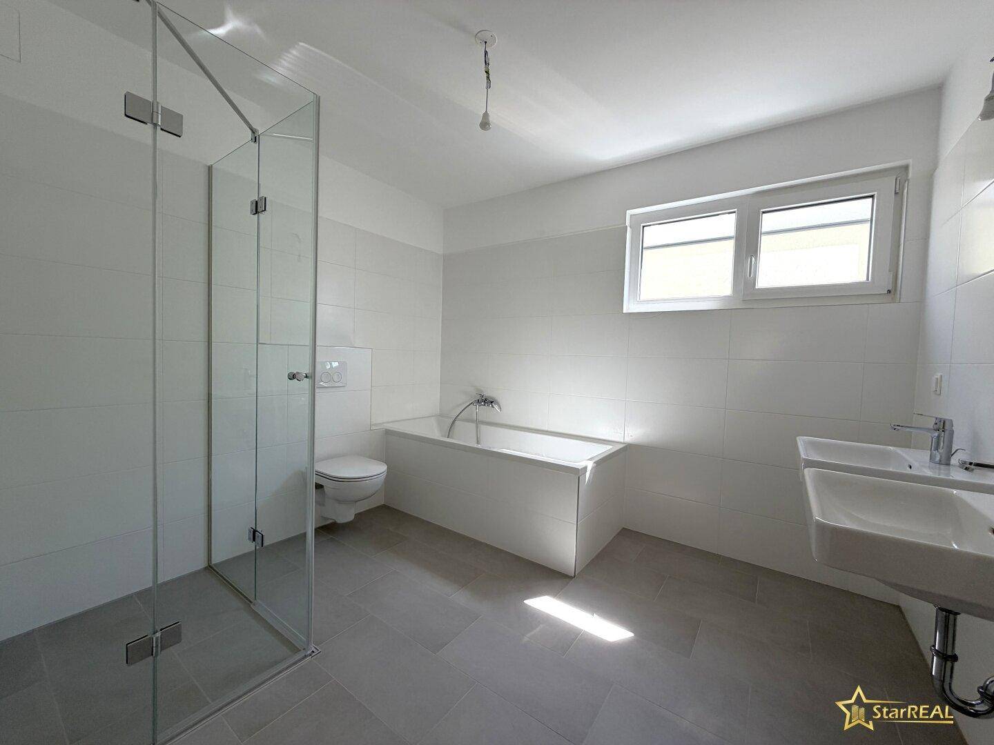 Helles Badezimmer mit Fenster, Duschkabine, Badewanne und Doppelwaschbecken.