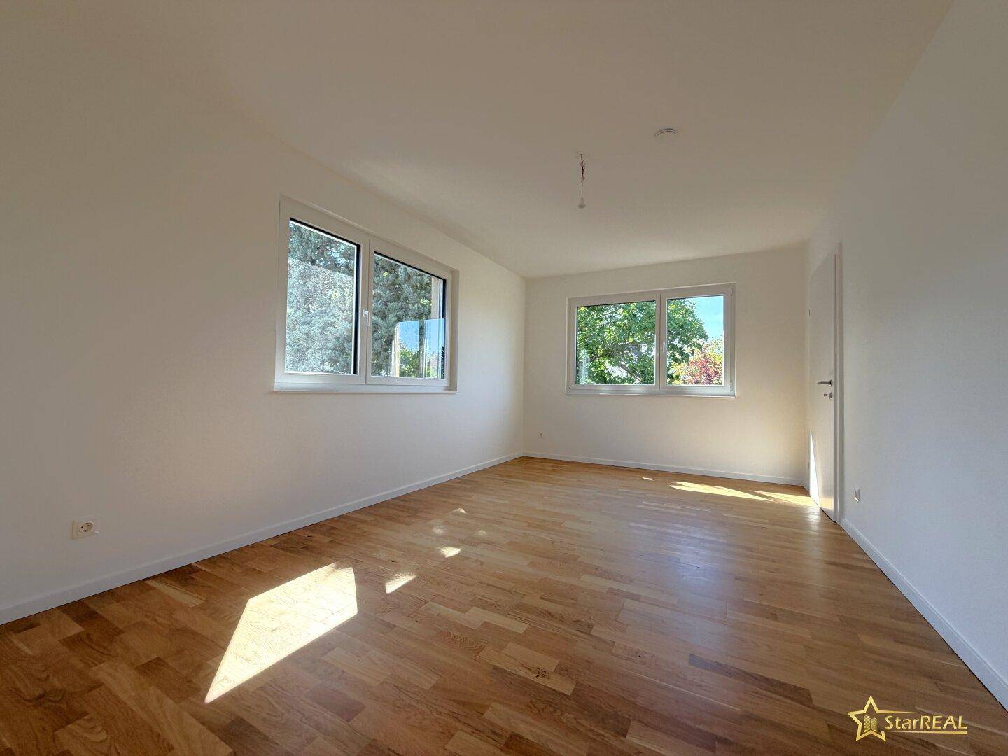 Helles Schlafzimmer mit Parkettboden und zwei Fenstern, die viel Tageslicht hereinlassen.
