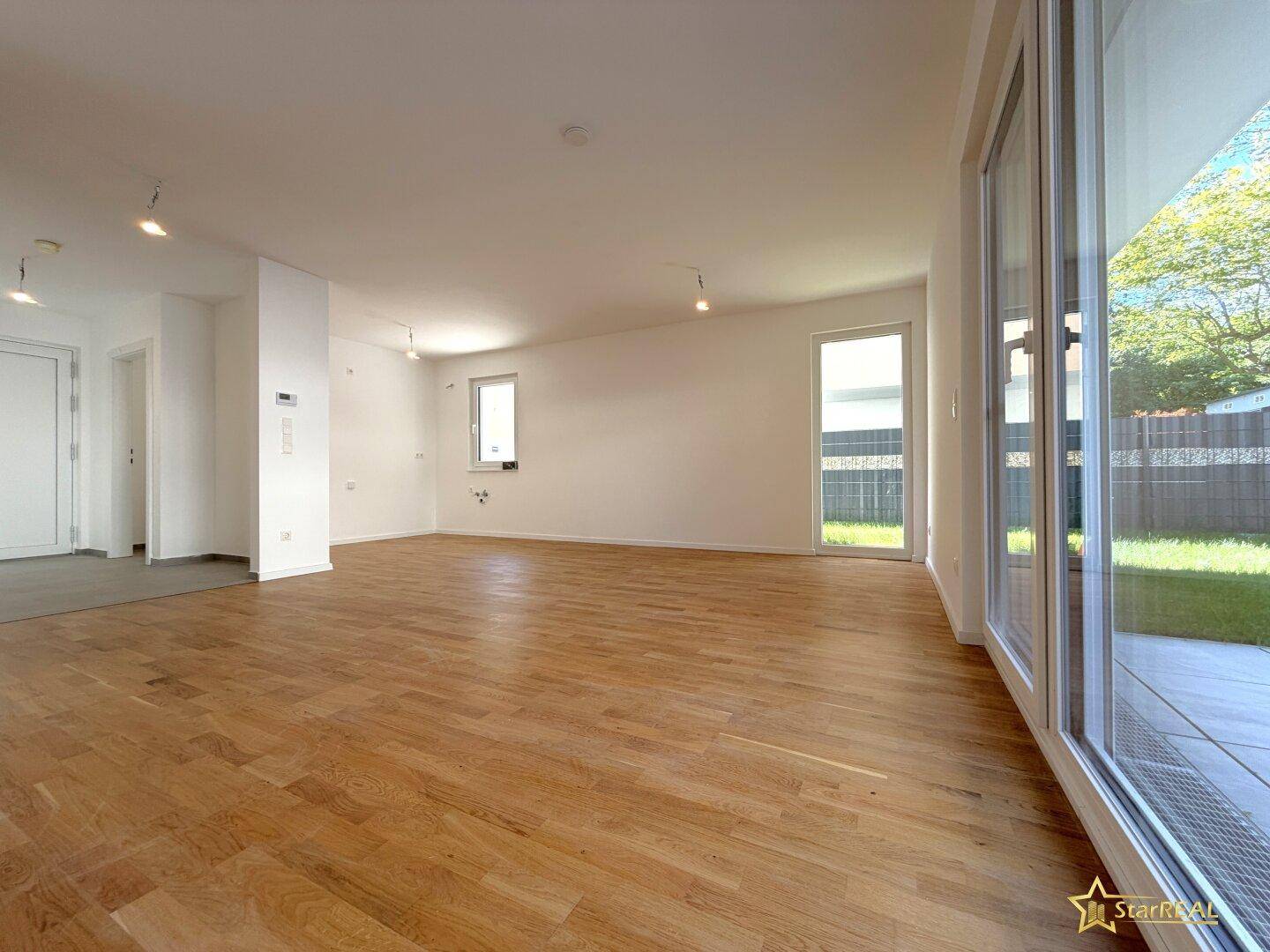 Geräumiges, leeres Wohnzimmer mit hellem Parkettboden und großen Fenstern zum Garten.