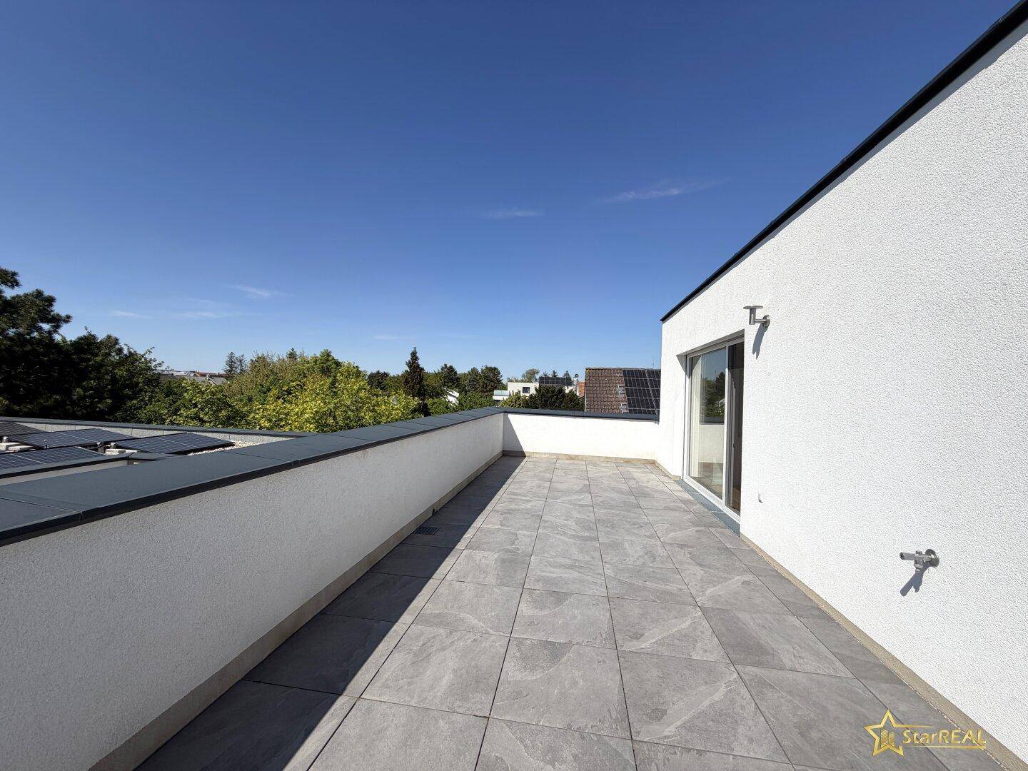 Geräumige Dachterrasse mit Fliesenboden und weitem Blick unter blauem Himmel.