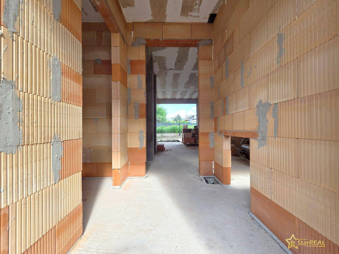 Langer Flur im Rohbau mit unverputzten Ziegelwänden und Betonboden.