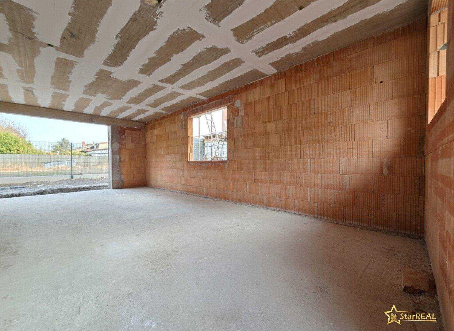 Geräumiger Rohbau-Raum mit Ziegelwänden, Betonboden und großer Fensteröffnung.