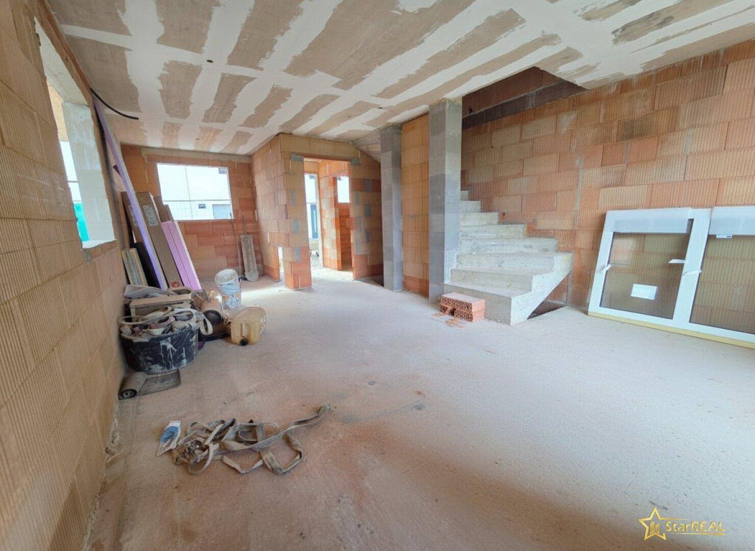 Innenraum im Rohbau mit sichtbarer Betontreppe und unverputzten Ziegelwänden.