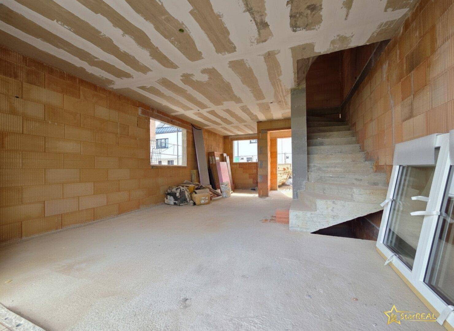 Rohbau-Raum mit Betontreppe, Ziegelwänden und Fensteröffnungen für natürliches Licht.