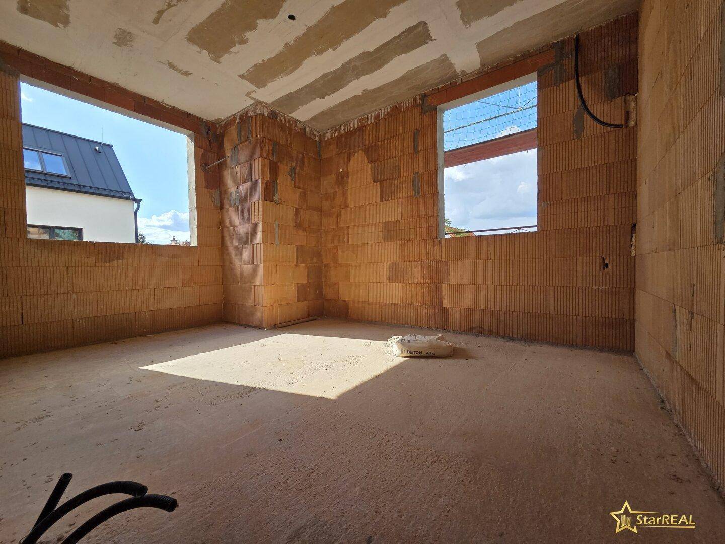 Schlafzimmer im Rohbau mit zwei Fensteröffnungen und unverputzten Ziegelwänden.