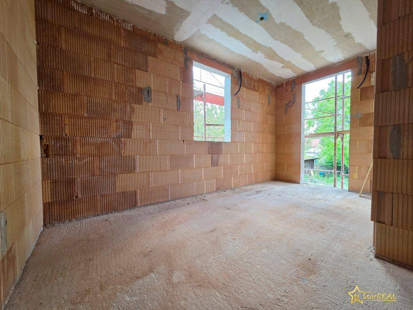 Helles Schlafzimmer im Rohbau mit Ziegelwänden und einer Fensteröffnung.