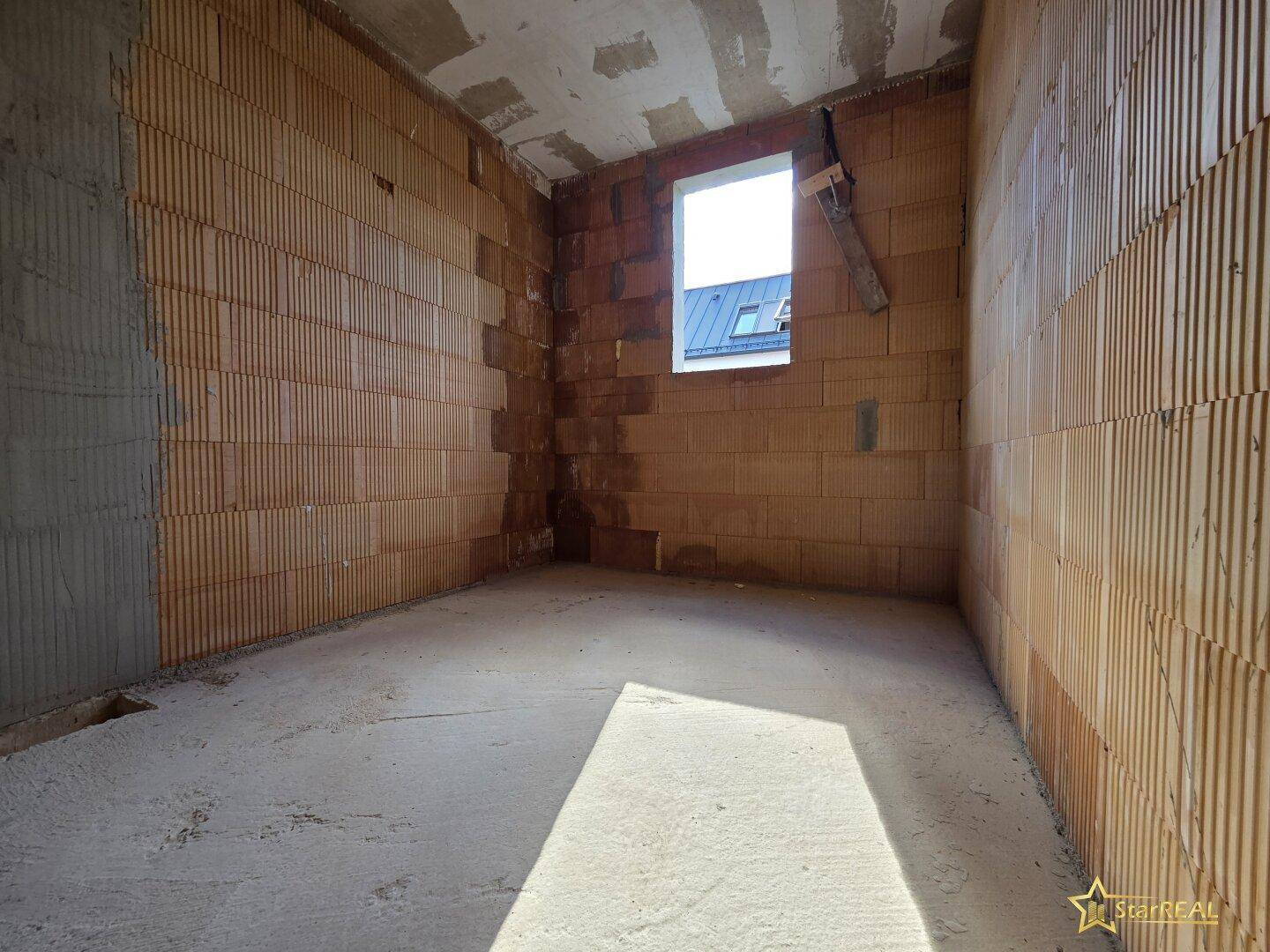Schlafzimmer im Rohbau mit Ziegelwänden, Betonboden und einer Fensteröffnung.