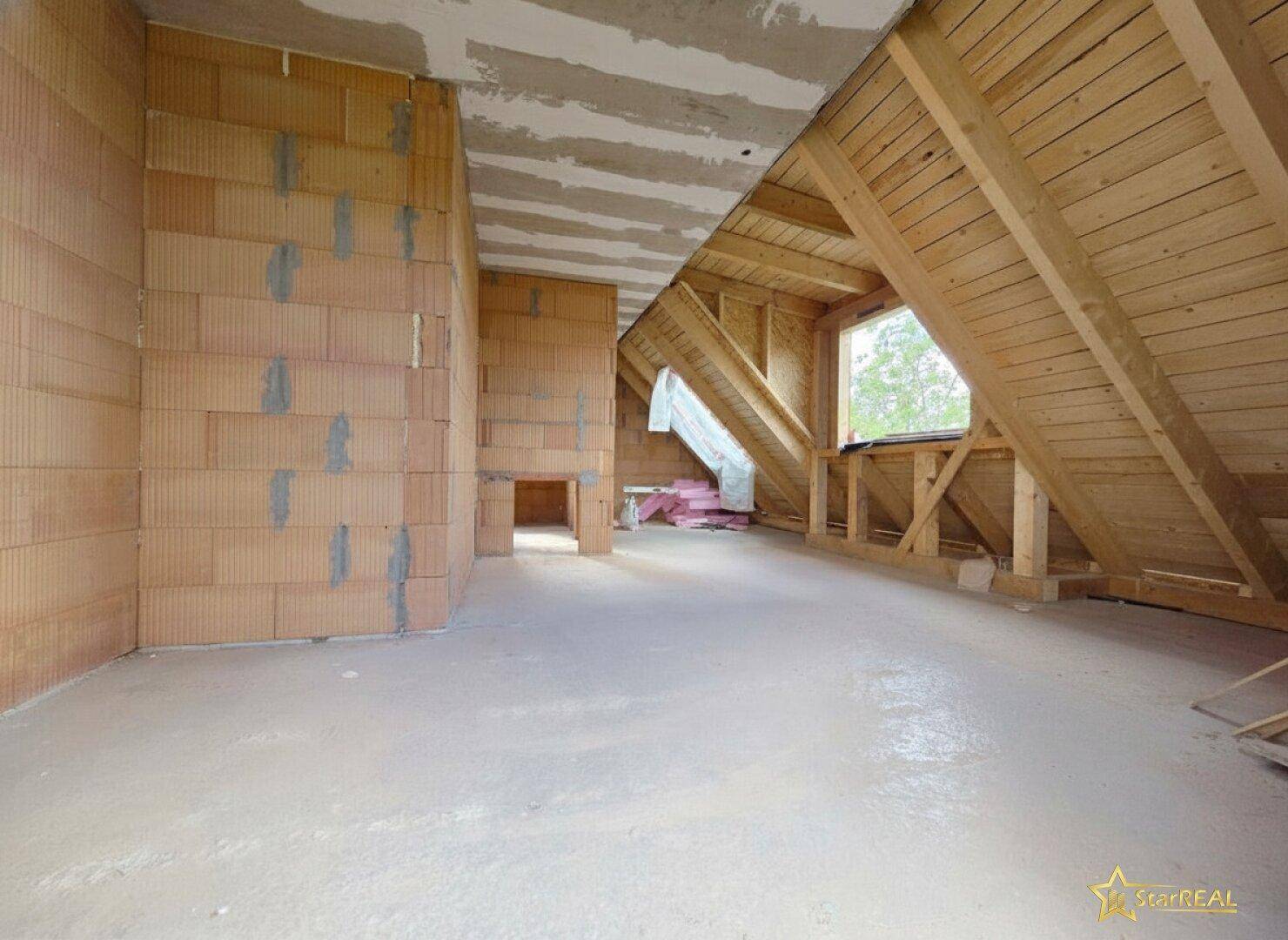 Dachgeschoss im Rohbau mit sichtbaren Holzbalken, Ziegelwänden und Fenster.