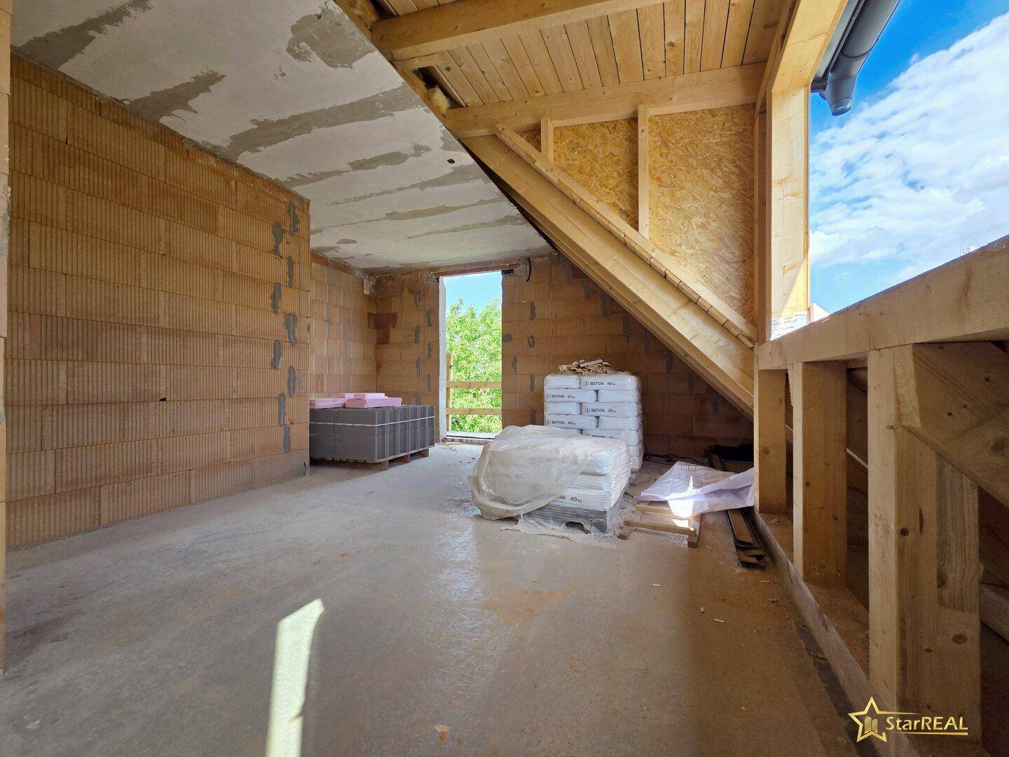 Dachgeschoss im Rohbau mit Holzbalken und Zugang zu einem zukünftigen Balkon oder einer Terrasse.