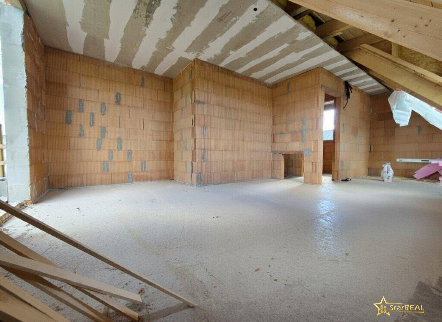 Geräumiges Dachgeschoss im Rohbau mit Ziegelwänden und Betonboden.
