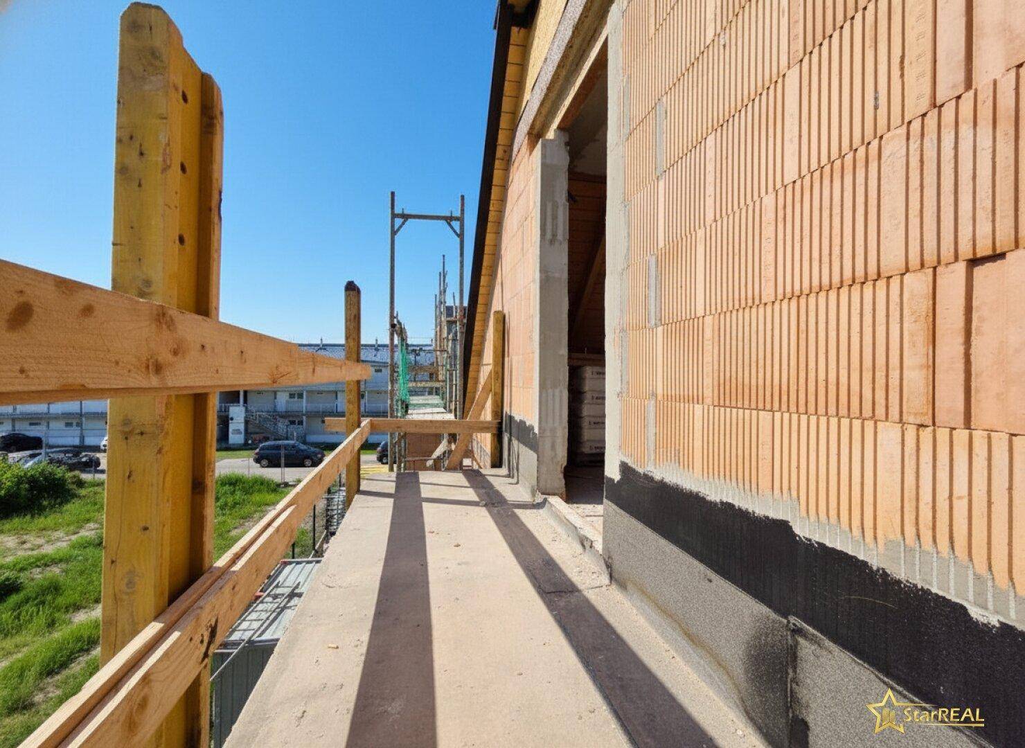 Baustelle mit einem provisorischen Balkon oder Laufsteg an der Fassade des Rohbaus.