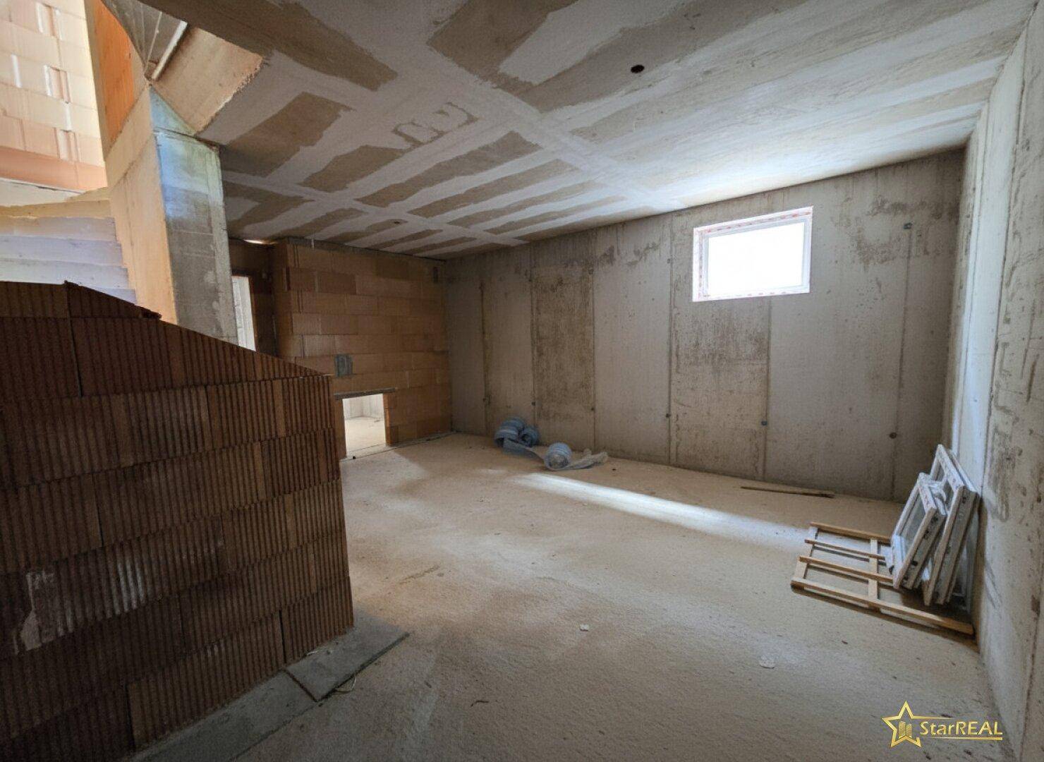 Kellerraum im Rohbau mit Betonwänden, Betonboden und einem kleinen Fenster.