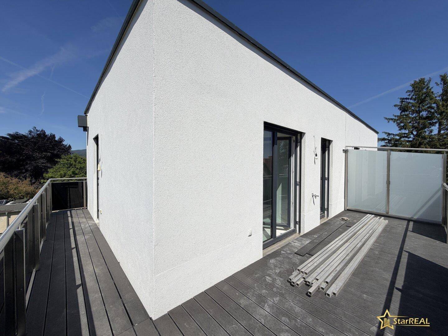 Geräumige Dachterrasse mit Holzdielen und moderner Glasbrüstung, noch im Bau befindlich.