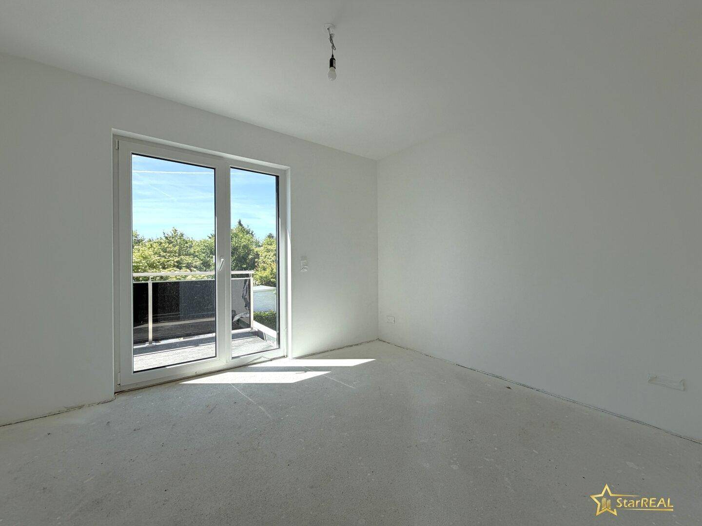 Helles Schlafzimmer im Rohbau mit Zugang zu einem Balkon und viel natürlichem Licht.