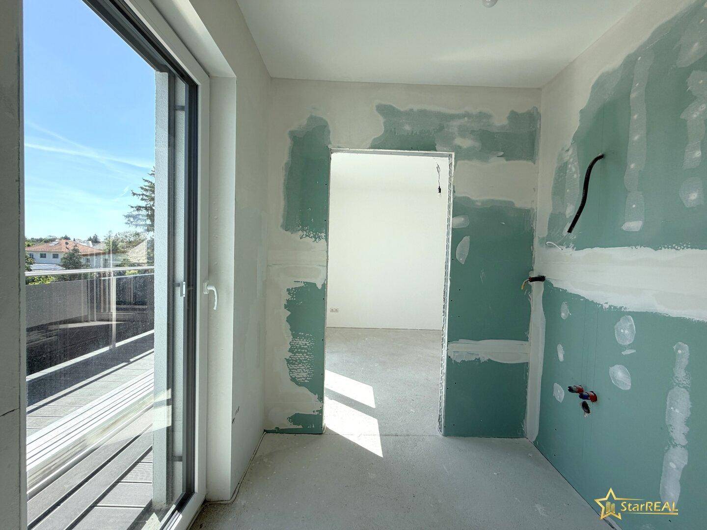 Badezimmer im Rohbau mit vorbereiteten Installationen und Zugang zu einem Balkon.