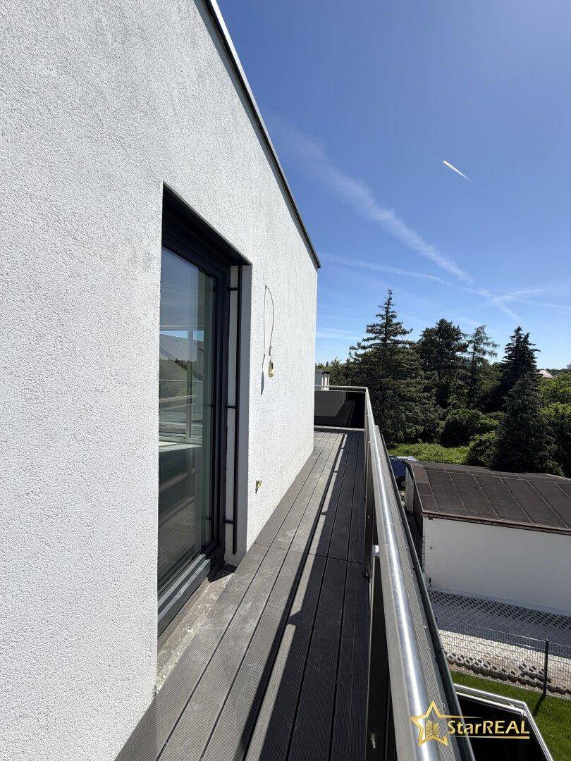 Langer Balkon mit Holzdielen und Metallgeländer, bietet einen weiten Blick ins Grüne.