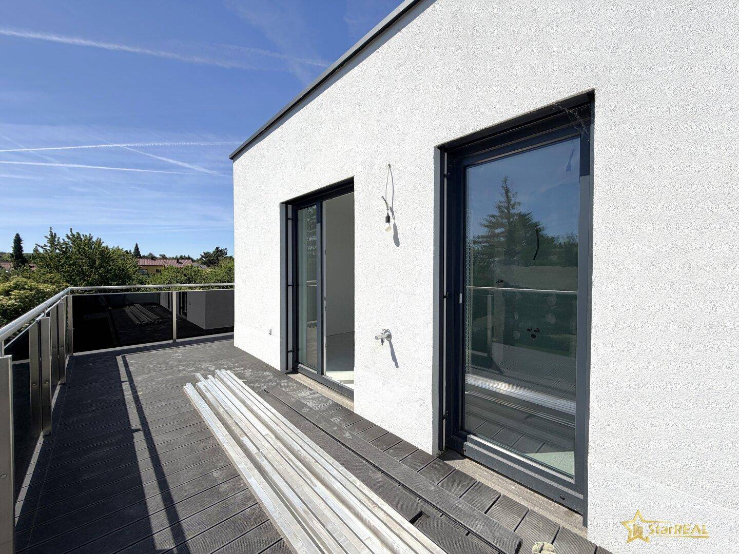 Moderne Dachterrasse mit dunklen Holzdielen und Glasbrüstung, noch im Bau befindlich.