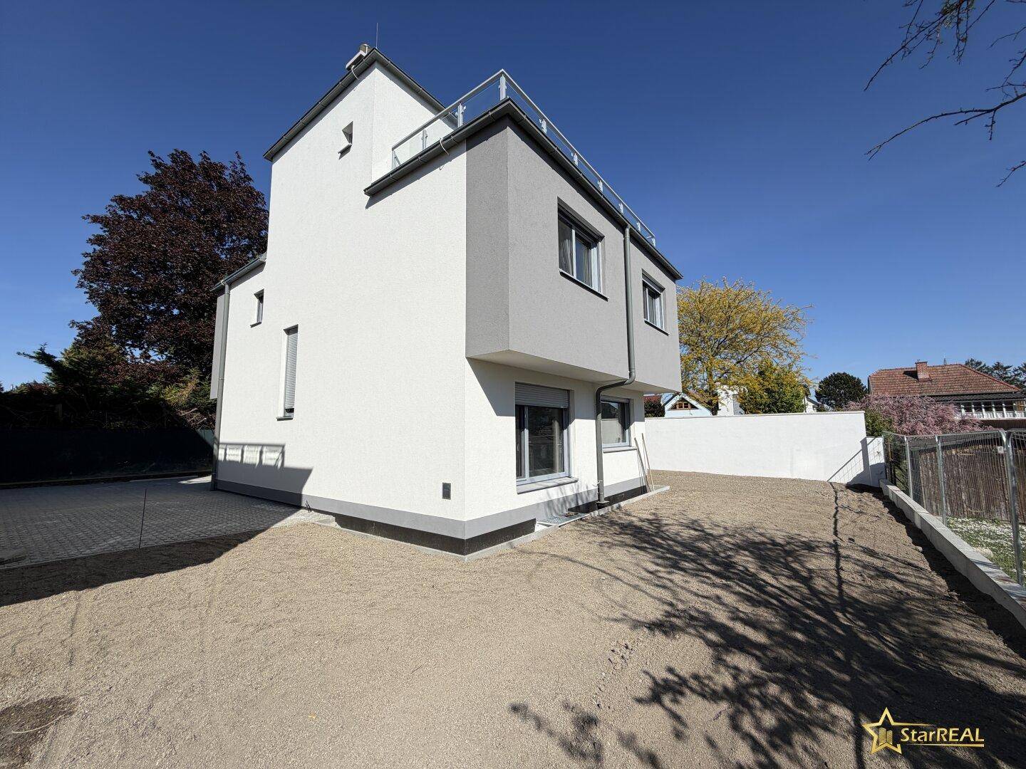 Moderne Reihenhausfassade in Weiß und Grau mit zukünftigem Gartenbereich.