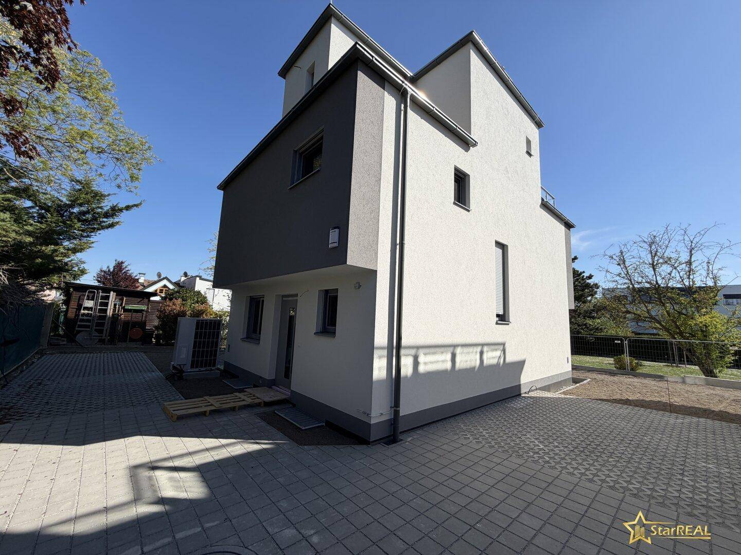 Moderne Hausfassade mit gepflastertem Bereich und Blick auf den Garten.