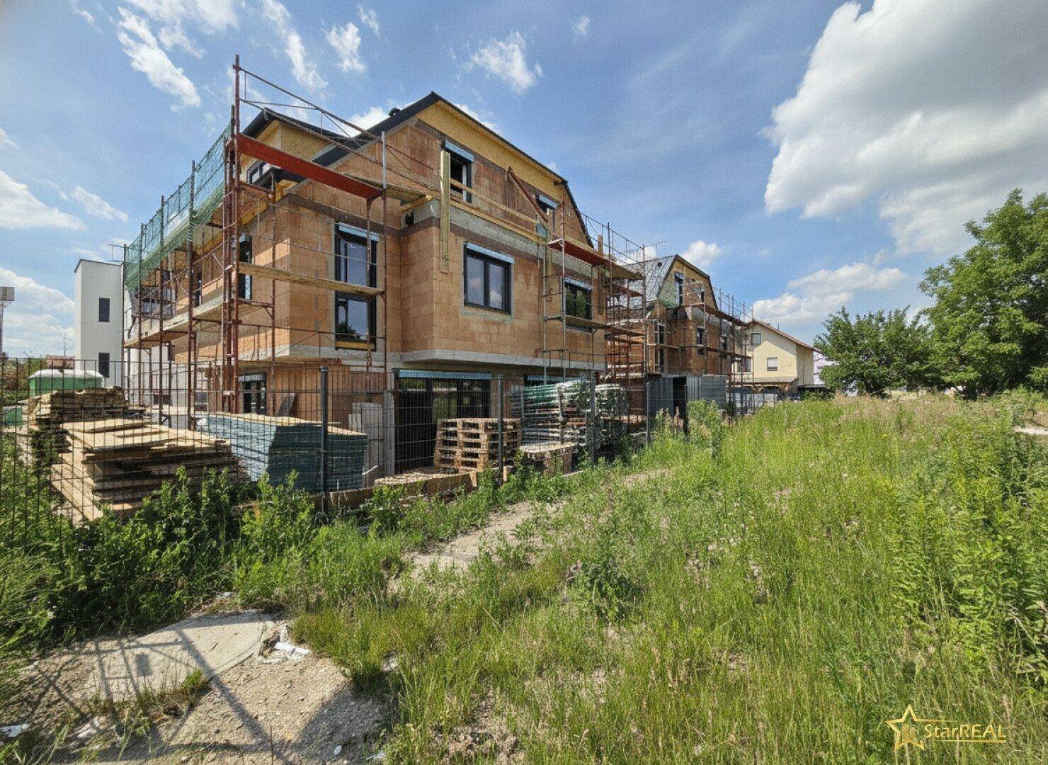 Neubau im Rohbauzustand mit Gerüst und Baumaterialien unter blauem Himmel.