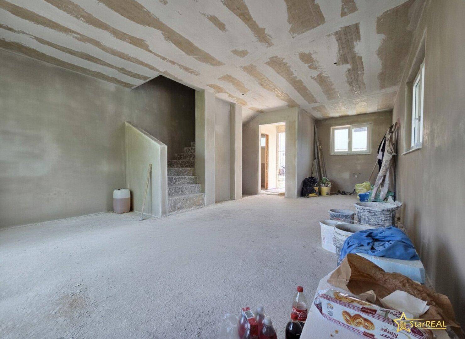 Geräumiger Wohnbereich im Rohbau mit Treppenaufgang und viel Potenzial für individuelle Gestaltung.