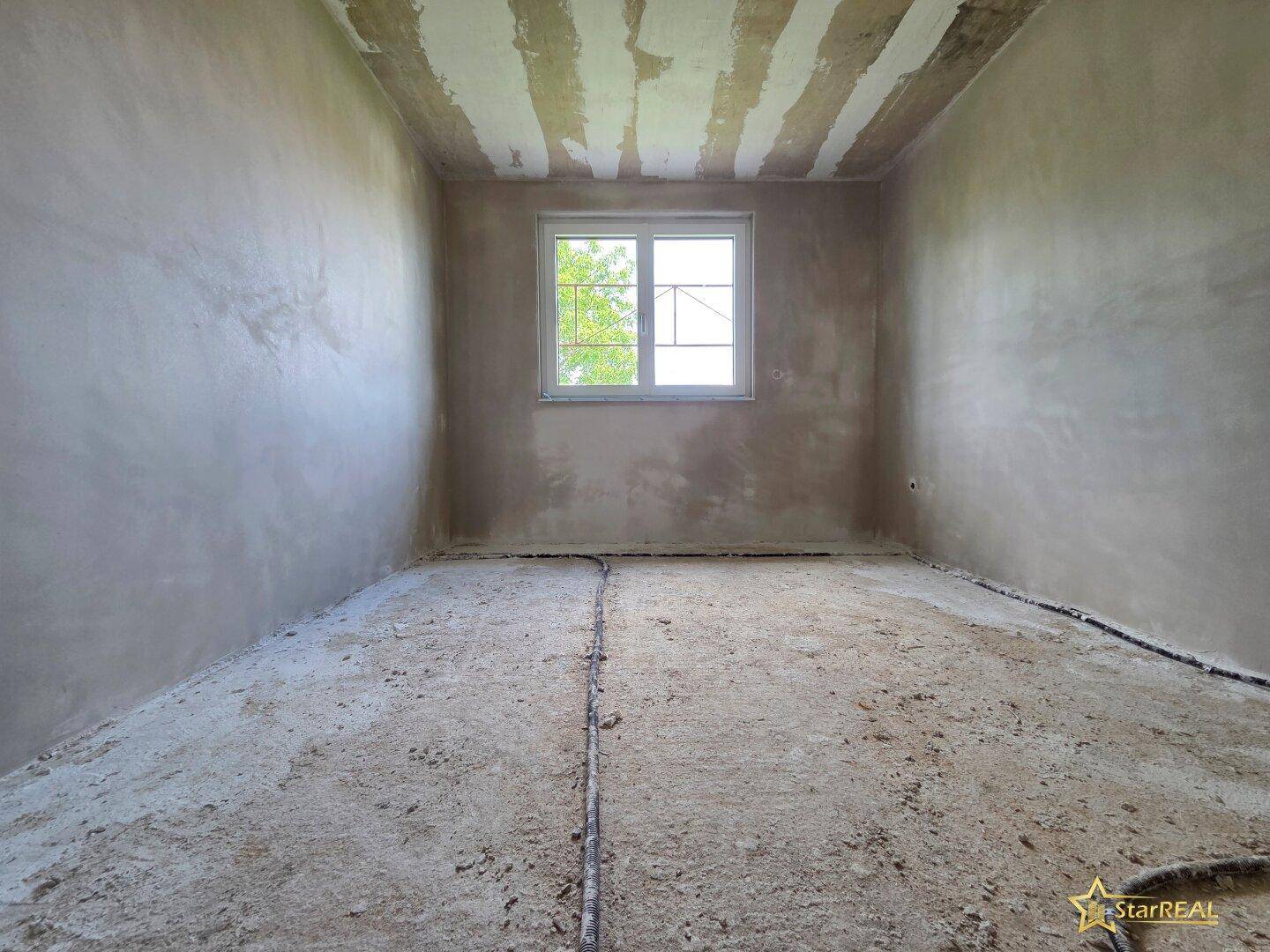 Kleinerer Raum im Rohbau mit einem Fenster, ideal als Kinderzimmer oder Büro.