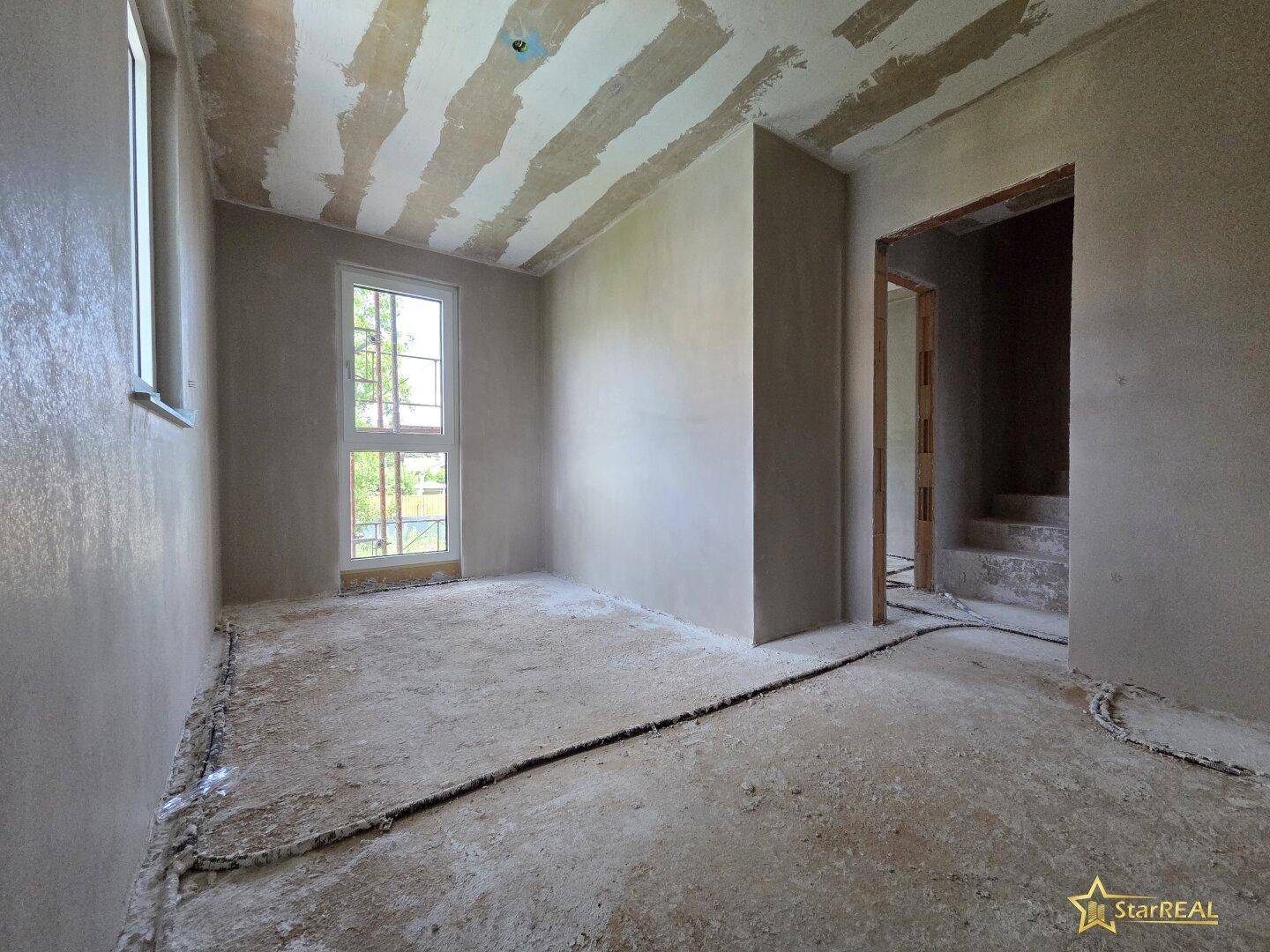 Unfertiges Zimmer im Rohbau mit einem hohen Fenster, das viel Licht spendet.