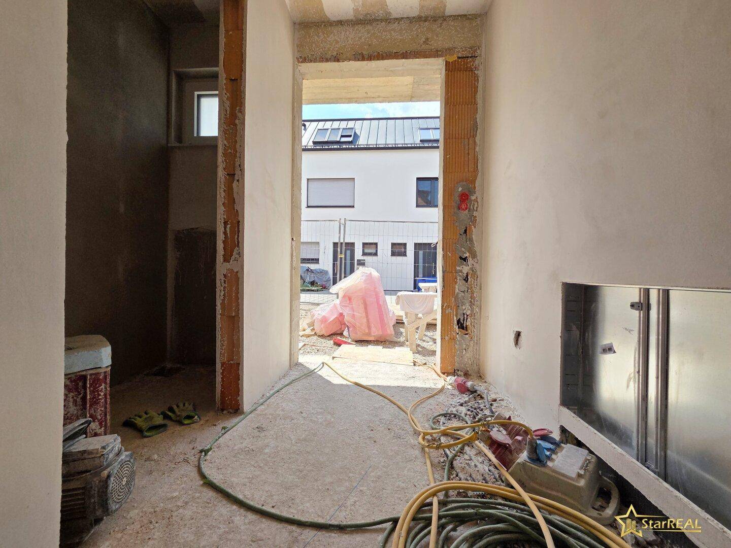 Flur im Rohbau mit Blick auf die Baustelle und die umliegenden Gebäude.