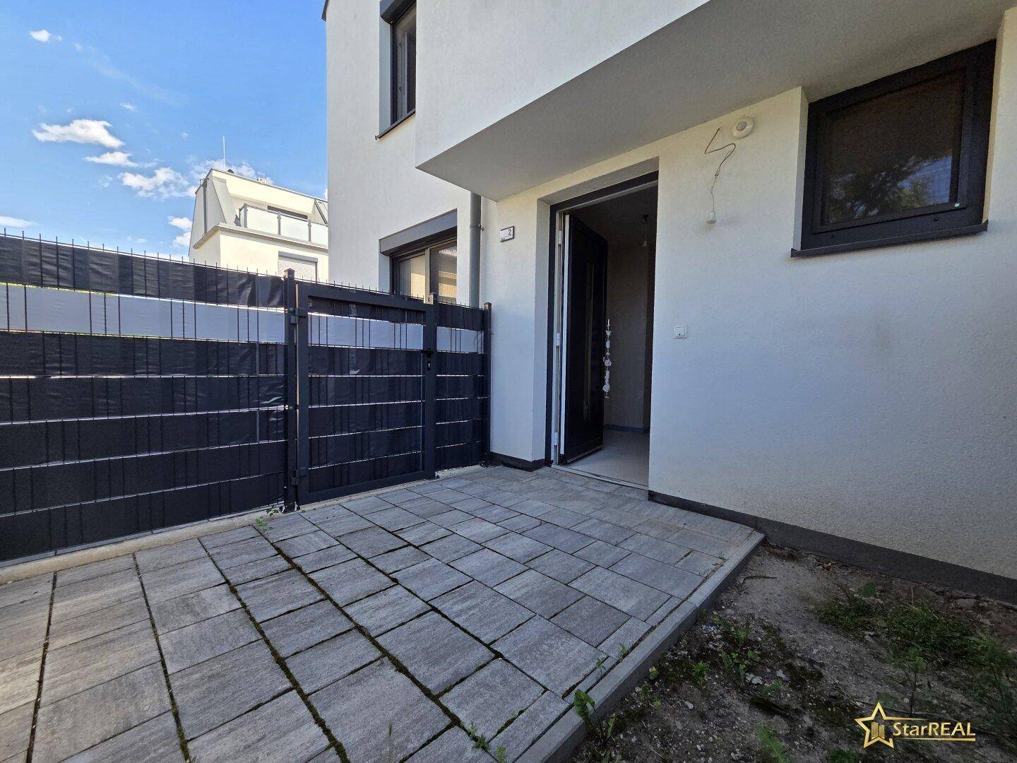 Eingangsbereich des Hauses mit gepflasterter Terrasse und moderner Haustür.
