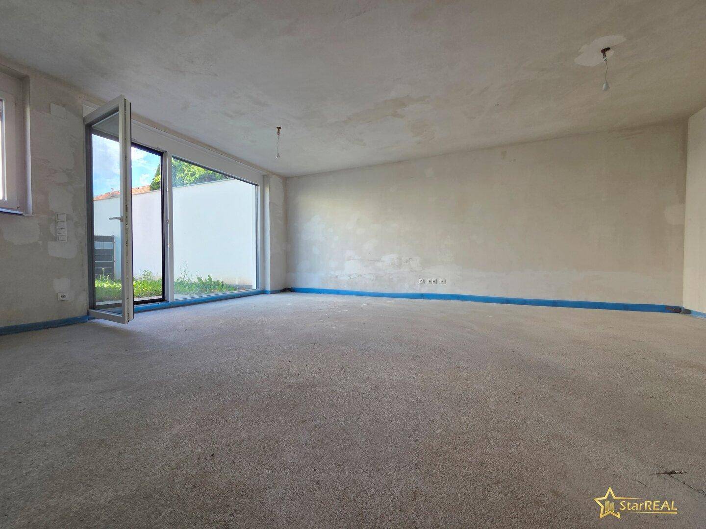 Heller, unfertiger Wohnraum mit großer Glastür zum Außenbereich.
