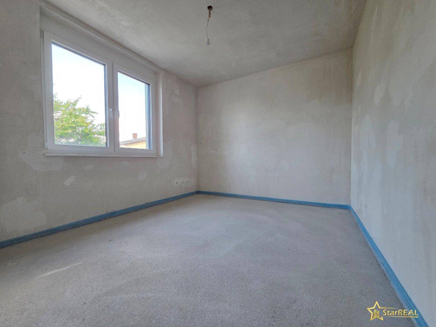 Helles, unfertiges Schlafzimmer mit großem Fenster und Rohbauzustand.